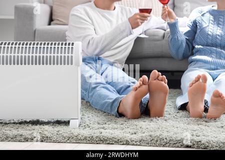 Barefoot young couple with wine warming near radiator at home, closeup Stock Photo
