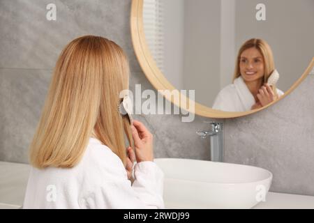 Beautiful woman brushing her hair near mirror in bathroom Stock Photo