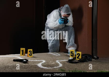 Criminologist in protective suit working at crime scene outdoors. Space for text Stock Photo