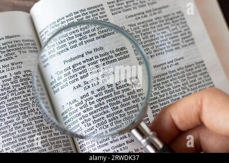 Ask, search, knock, biblical text verse. Human hand holding a magnifying glass over Holy Bible Book. Close-up. Stock Photo