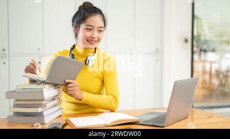 A beautiful young Asian female university student is searching for information in a book, working on her school project, preparing for an exam, and do Stock Photo