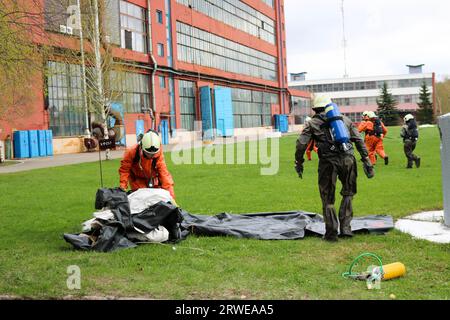 Professional firefighters, rescuers in protective fireproof suits, white helmets and gas masks are preparing to rescue people from the industrial buil Stock Photo