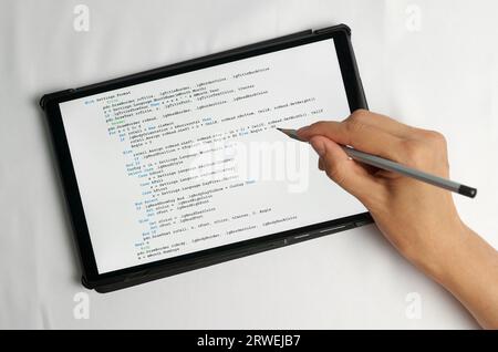 Programming and coding concept. A hand with a pencil writes a program listing on the screen Stock Photo