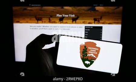 Person holding cellphone with logo of US agency National Park Service (NPS) on screen in front of business webpage. Focus on phone display. Stock Photo
