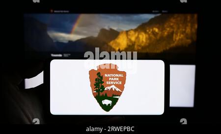 Person holding smartphone with logo of US agency National Park Service (NPS) on screen in front of website. Focus on phone display. Stock Photo