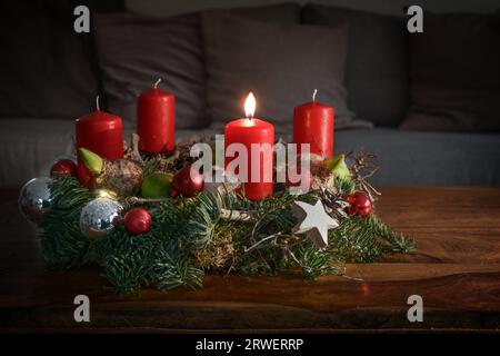 Advent wreath with one burning red candle and Christmas decoration on a wooden table in front of the couch, festive home decor for the first Sunday, c Stock Photo