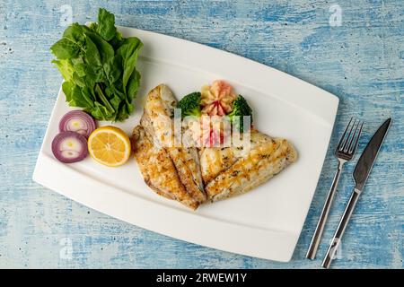 Grilled sea bream with vegetables and greens on wooden table Stock Photo