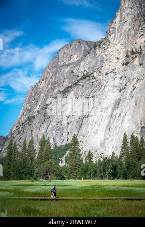 Two people walking through Yosemite valley meadow with majestic mountains in background. California, USA Stock Photo
