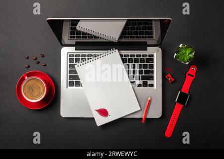 Blank notepad over laptop, watch and coffee cup on office black table. Top view. Stock Photo