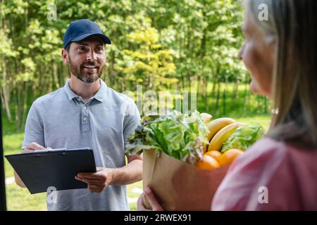 Courier service worker delivering fresh food to woman client signing some documents. Stock Photo