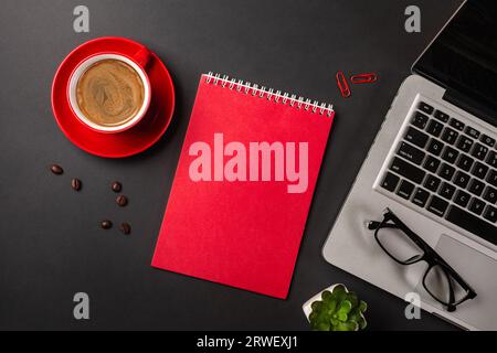 Blank notepad over laptop and coffee cup on office black table. Top view with copy space. Stock Photo