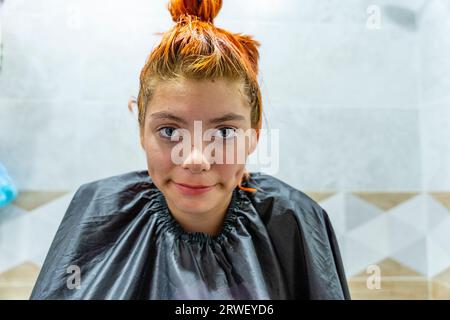 a teenage girl dyes her hair red. The process of dyeing hair red. Self-coloring of hair at home. Stock Photo