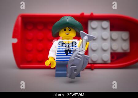 Small fisherman with a fish, red boat in the background Stock Photo