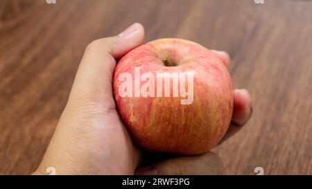 Fresh red apple fruit held in hand on wooden table Stock Photo