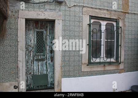 Vintage looking Front Door with Distressed Paintwork and Window patterned Metal Grill, surrounded with Green& White Patterned Portuguese Wall Tiles. Stock Photo