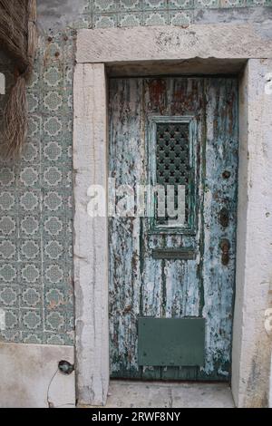 A Vintage looking Front Door with Distressed Paintwork and patterned Metal Grill, surrounded with Green and White Patterned Portuguese Wall Tiles. Stock Photo