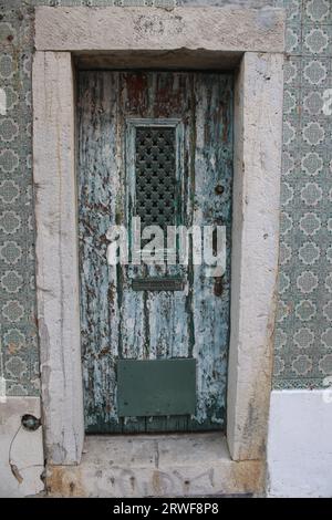 A Vintage looking Front Door with Distressed Paintwork and patterned Metal Grill, surrounded with Green and White Patterned Portuguese Wall Tiles. Stock Photo