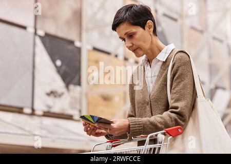 Portrait of mature woman choosing paint colors and holding samples in home improvement store, copy space Stock Photo