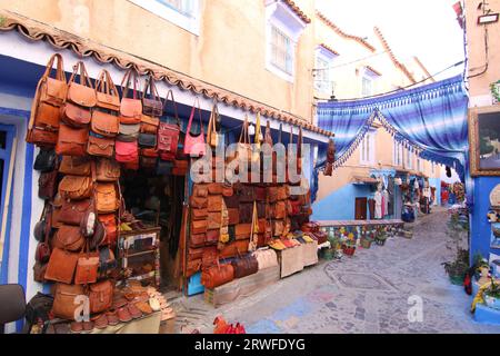 A shop front displaying handmade leather bags outside, in a row of other shops in the narrow alleys painted blue in the streets of  Chefchouen. Stock Photo