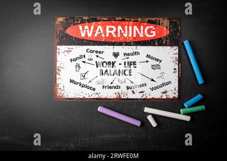 Work Life balance concept. Metal warning sign and colored pieces of chalk on a dark chalkboard background. Stock Photo