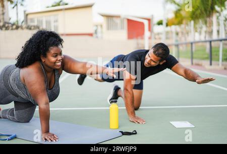 African curvy woman and personal trainer doing functional workout training session outdoor - Sport and healthy lifestyle concept - Main focus on girl Stock Photo