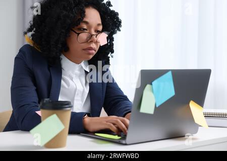 Deadline concept. Tired woman working with laptop in office. Many sticky notes everywhere as reminders Stock Photo