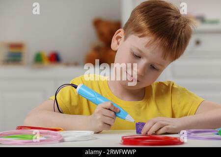 Boy drawing with stylish 3D pen at white table Stock Photo