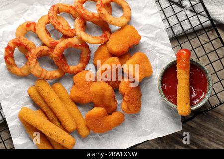 Tasty chicken nuggets, fried onion rings, cheese sticks and ketchup on wooden table, top view Stock Photo