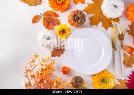 Autumn holiday table setting. Thanksgiving holiday menu, greeting card. White kitchen table with plate and cutlery, fall leaves, flowers and decor fla Stock Photo