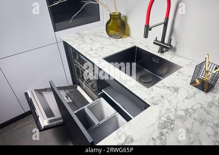 Kitchen with built-in opened dishwasher and pull out drawer for waste bin separate waste collection. Water faucet sink built in compact high pressure Stock Photo