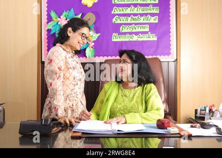 School Principal mam checking some important documents in a file with her personal assistant, discussion, signing the documents, progress in education Stock Photo