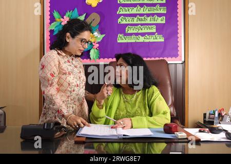 School Principal mam checking some important documents in a file with her personal assistant, discussion, signing the documents, progress in education Stock Photo