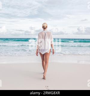 Woman wearing white loose tunic over bikini on Mahe Island, Seychelles. Summer vacations on picture perfect tropical beach concept. Stock Photo