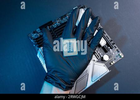 a computer processor in a gloved hand against the background of the motherboard. Accessories and computer equipment. Central processing chip or microp Stock Photo