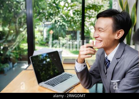 Young businessman laughing with a colleague while sitting on a chair in a modern office. Funny positive emotions at work. Stock Photo