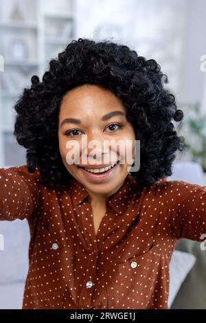 Close-up vertical photo. A young African American smiling woman is smiling and talking to the camera online on a video call. Stock Photo