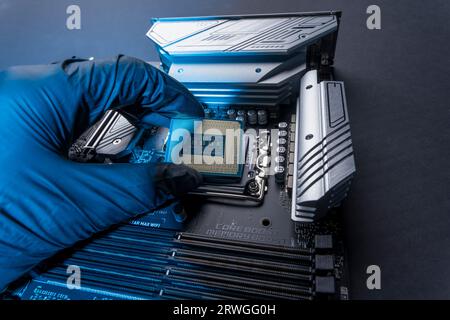 a computer processor in a gloved hand against the background of the motherboard. Accessories and computer equipment. Central processing chip or microp Stock Photo