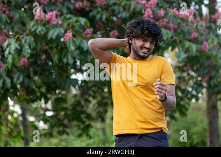 Indian young man walks in the park, does sports. Suffering from itching and mosquito bites, grimacing from discomfort. Stock Photo