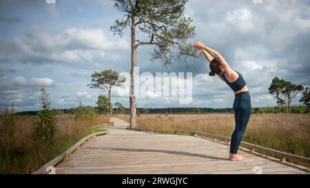 Fit, sporty woman practicing yoga on a boardwalk, doing a backbend. Stock Photo