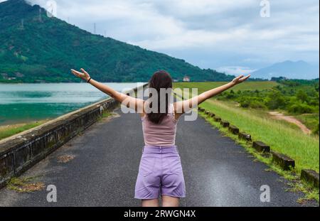 Young russian woman traveler with opened arms near lake and mountains in Khanh Hoa Province, Vietnam Stock Photo