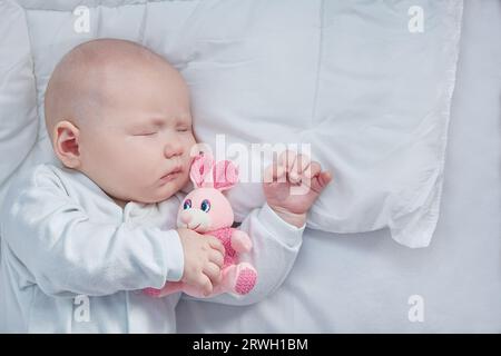 Cute baby sleeps with his toy knitted pink bunny. The concept of a new family and child protection. Copy space Stock Photo