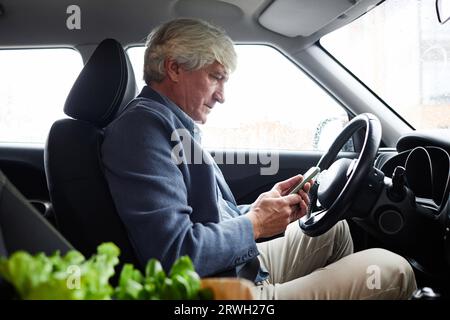Side view portrait of senior man using smartphone app in car, copy space Stock Photo