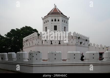 A white fort-like structure with a red roof, surrounded by a wall with black crosses, stands against a backdrop of trees and a clear sky. Stock Photo