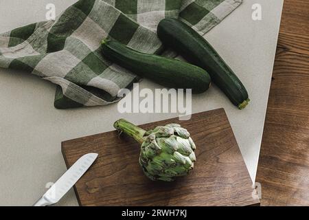 Zucchini and artichoke on wooden board, linen towel and stainless still kitchen knife. Healthy food cooking ingredients background with fresh vegetabl Stock Photo