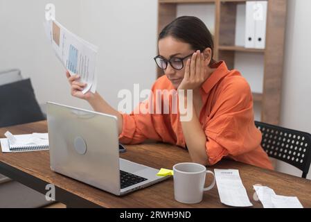 Woman with papers pays domestic bills online using computer app making credit insurance payment Stock Photo