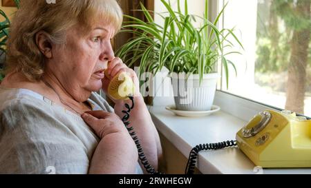 Old woman receives phone call. Grandmother talking on an old disc phone ...