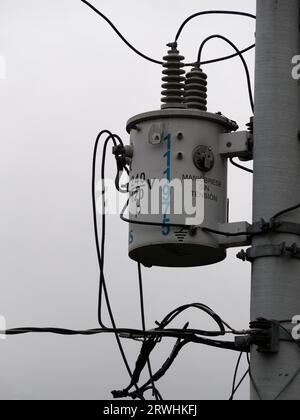 electric transformer of a city utility hanging on a pole with maintenance signs in Spanish and ceramic insulators Stock Photo