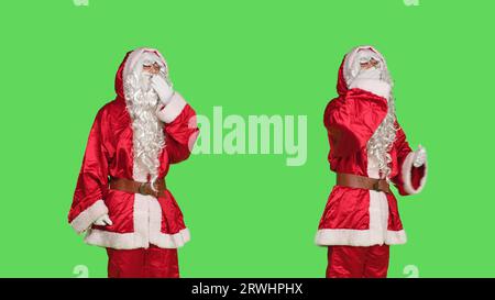 Sweet santa claus sends air kisses in studio, doing romantic gesture over greenscreen backdrop. Young man in saint nick costume acting flirty and admire people, christmas eve concept. Stock Photo