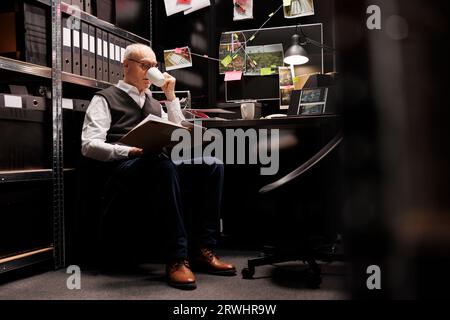 Elderly private detective checking mysterious missing case, analyzing victim profile report in arhive room. Senior investigator working late at night at criminology department documents Stock Photo