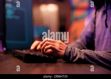Hacker hands writing virus software code and typing on keyboard. Young internet criminal programming ransomware and cracking password to break into computer system with close up on arms Stock Photo